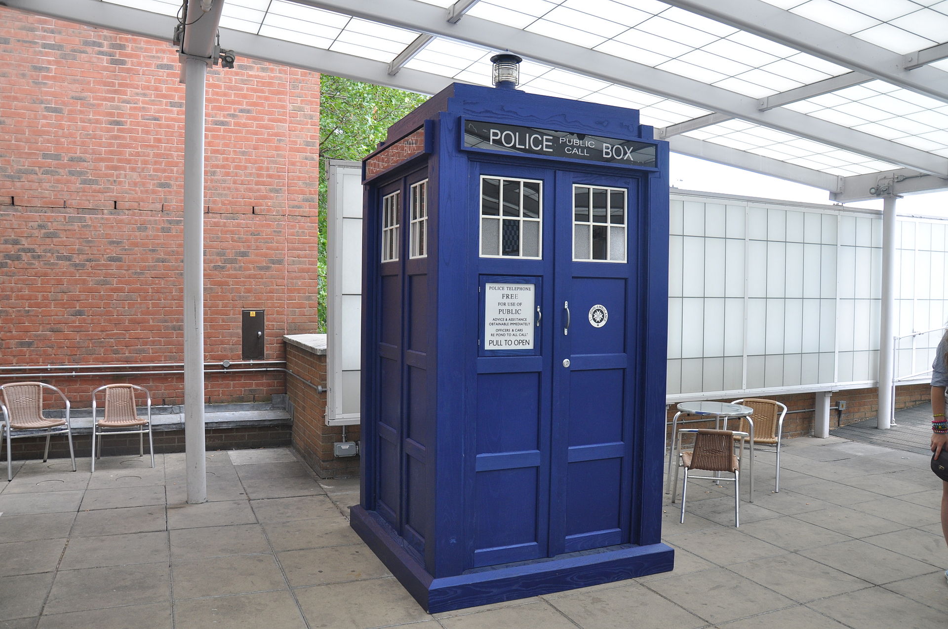 a TARDIS placed in an outdoor sitting area with a backdrop of a brick wall